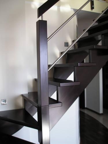 Ciemne, drewniane schody z metalową balustradą, widok z dołu, minimalistyczny design, oświetlenie punktowe na ścianie.