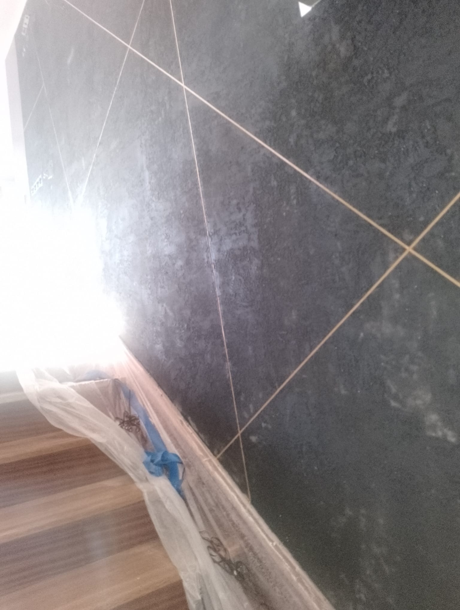 Ciemna, matowa płytka ścienna z jasnymi fugami ułożona pod kątem, zabezpieczona folią malarską u podstawy schodów.