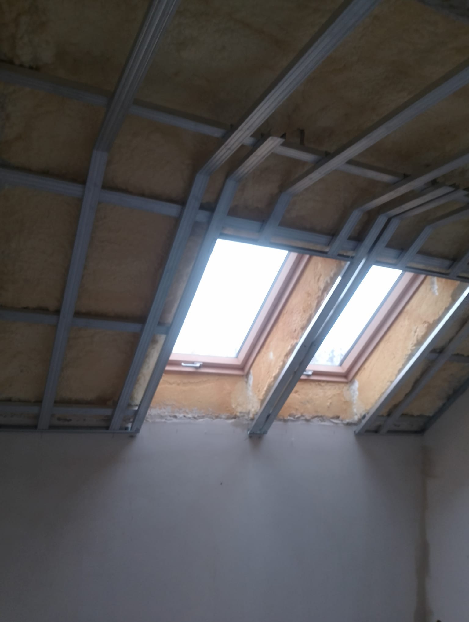 Montaż metalowego stelażu pod płyty kartonowo-gipsowe na poddaszu, widoczne ocieplenie i okna dachowe.