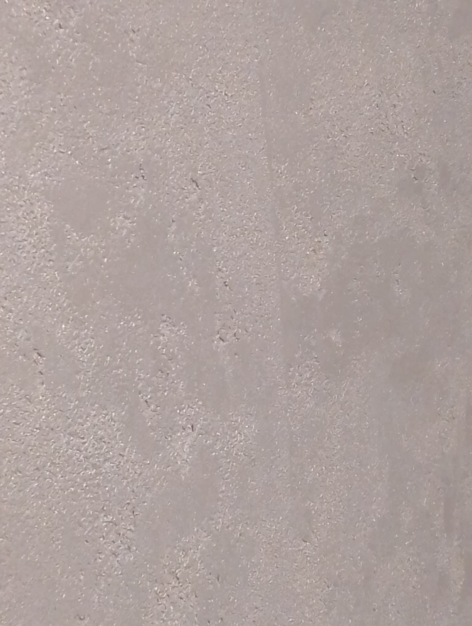 Szara, drobnoziarnista faktura ściany, przypominająca tynk dekoracyjny z bliska.