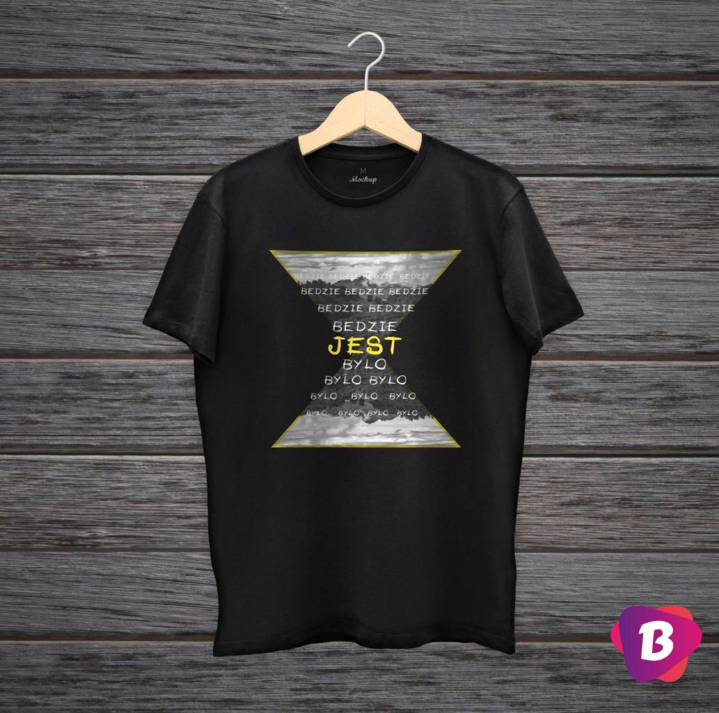 Czarny t-shirt z nadrukiem w kształcie klepsydry, zawierającym słowa 'Będzie', 'Jest' i 'Było', wiszący na drewnianym wieszaku na tle drewnianej ściany.