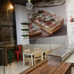 Wnętrze pizzerii w Piotrkówku Dużym z plakatem pizzy na ścianie, stoliki dla gości i witryna chłodnicza z blatem z drewna.