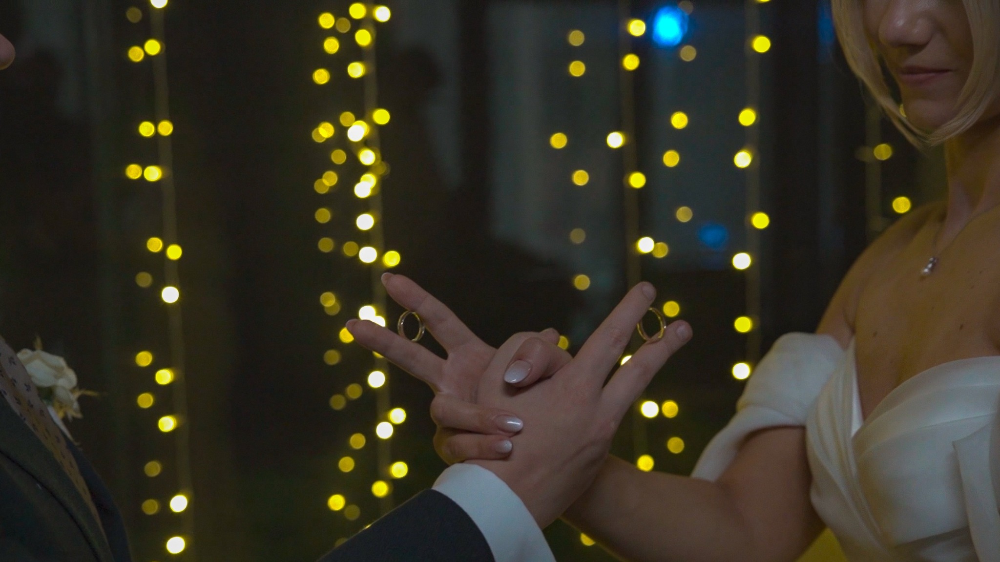 Obrączki ślubne na palcach pary młodej w Krakowie, na tle dekoracji świetlnych. Ujęcie z bliska, skupione na dłoniach i symbolice małżeństwa.
