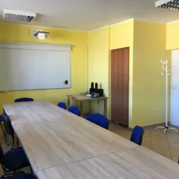 Sala lekcyjna w Białymstoku z długim stołem, krzesłami, tablicą i projektorem, przygotowana do zajęć językowych.