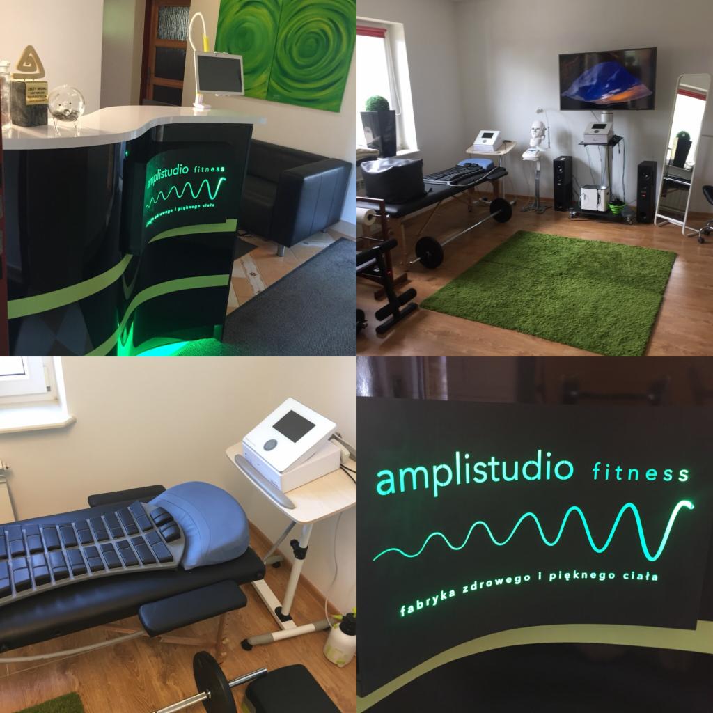 Wnętrze studia fitness z recepcją, sprzętem do ćwiczeń i logo 'amplistudio fitness' podświetlonym na zielono.