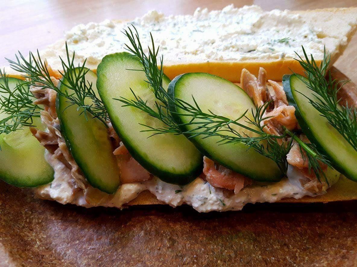 Otwarta kanapka z łososiem, kremowym serkiem, plastrami ogórka i świeżym koperkiem na drewnianej desce.