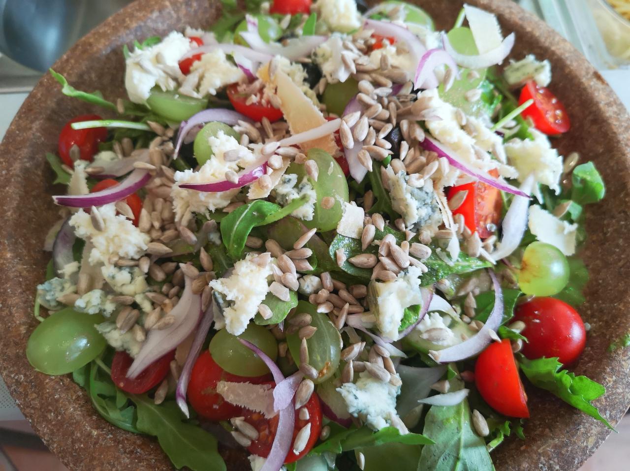 Sałatka z rukoli, winogron, pomidorów cherry, czerwonej cebuli, sera pleśniowego i pestek słonecznika w rustykalnej, kamionkowej misce.