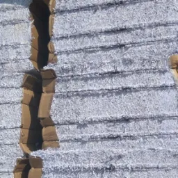 Paczki pociętych dokumentów sprasowane w kartonach, ułożone warstwami, widoczne metalowe elementy mocujące.