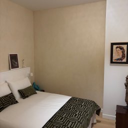 LCITB Tymoteusz Wiśniowski - Beżowa sypialnia z łóżkiem, obrazem na ścianie i lampą z wikliny. Ściany z fakturą, drewniana podłoga. Przytulne wnętrze po remoncie.