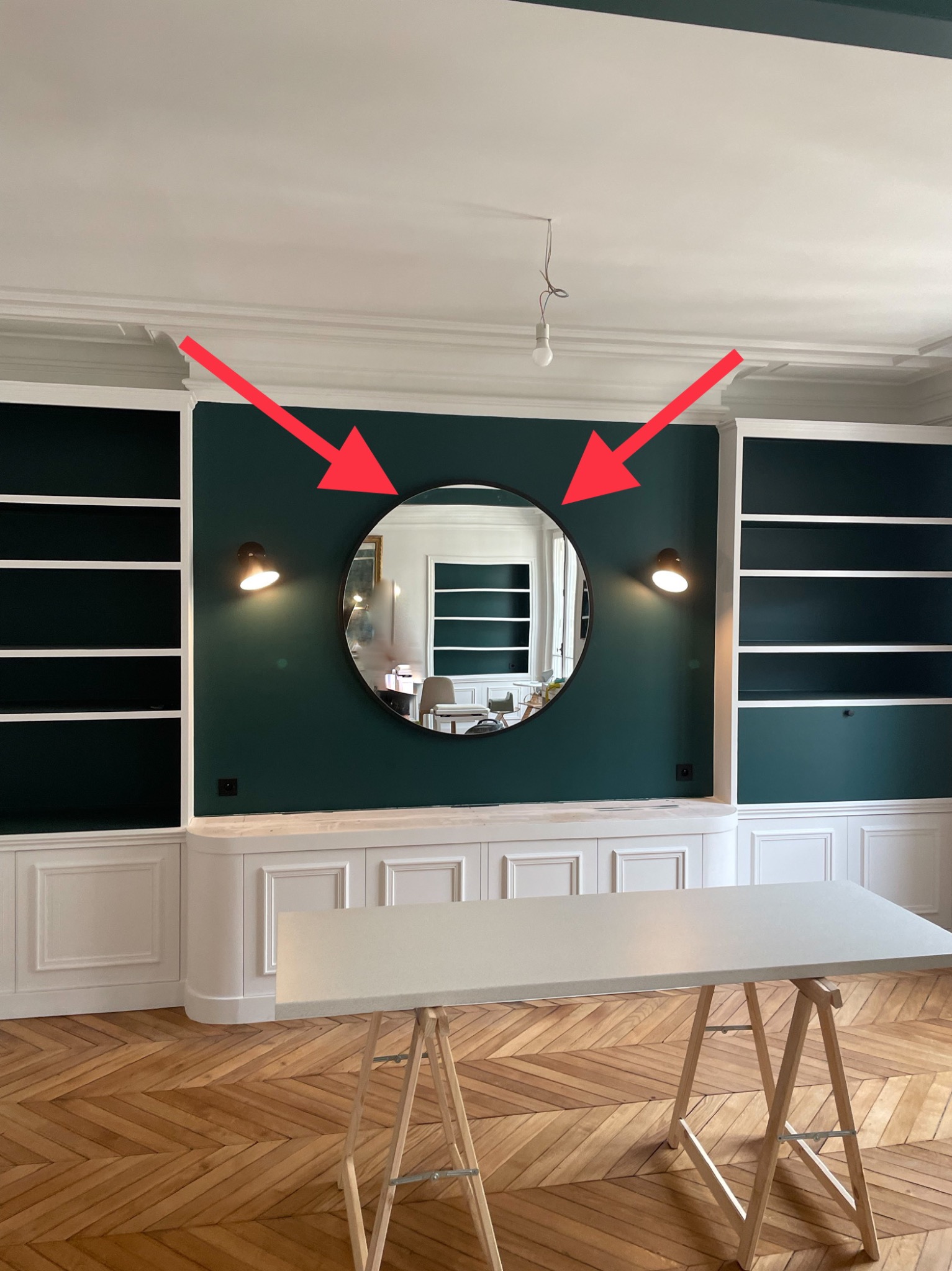 Eleganckie wykończenie wnętrza: ciemnozielona ściana z okrągłym lustrem i kinkietami, białe zabudowy, parkiet w jodełkę. Widoczny stół warsztatowy.