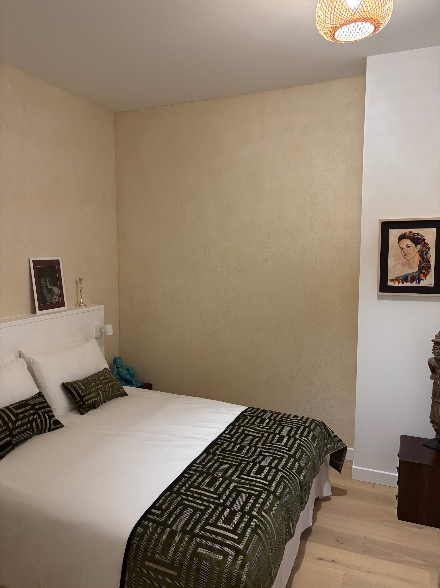 Beżowa sypialnia z łóżkiem, obrazem na ścianie i lampą z wikliny. Ściany z fakturą, drewniana podłoga. Przytulne wnętrze po remoncie.