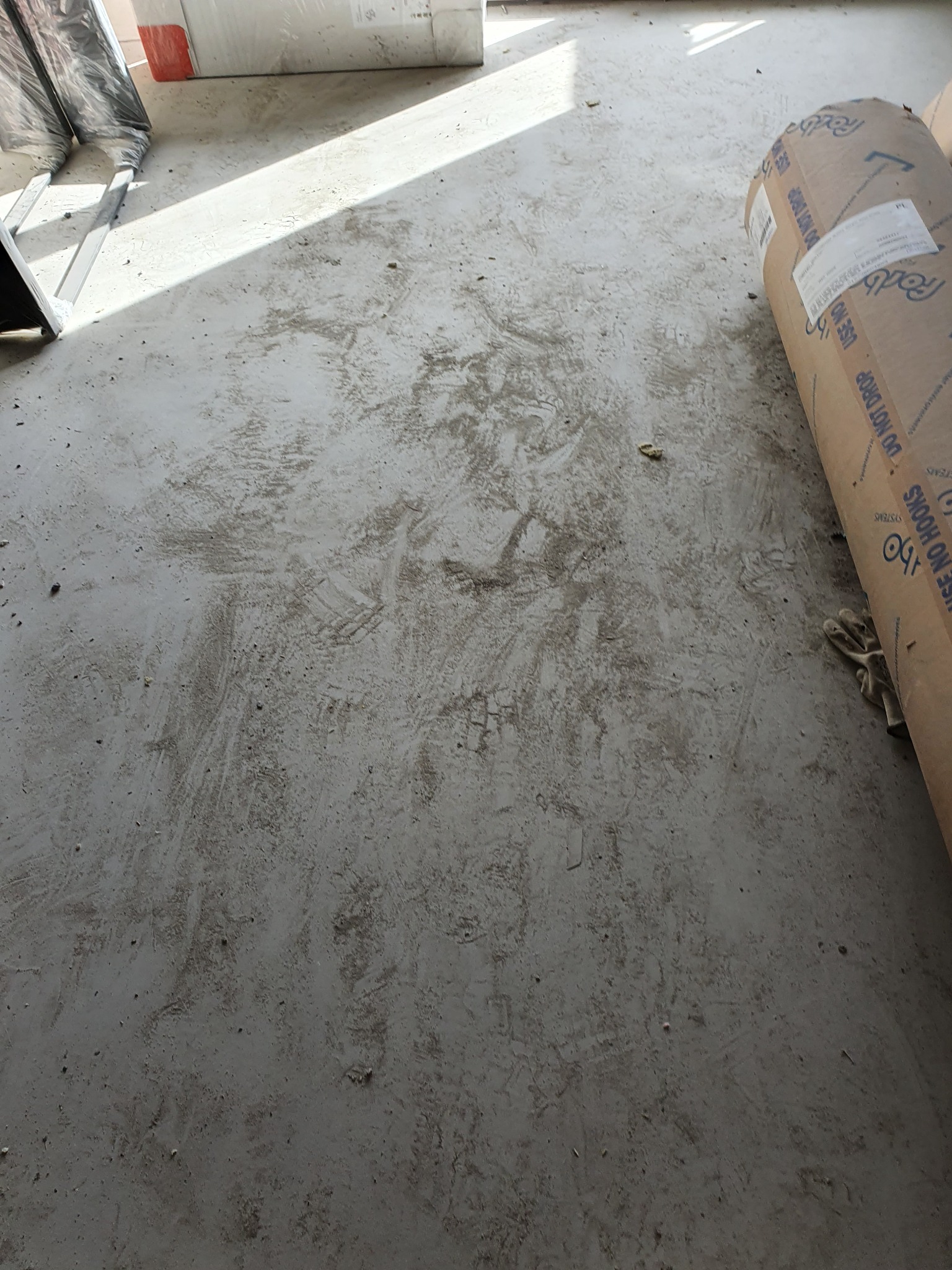 Brudna podłoga w trakcie sprzątania po remoncie, widoczne ślady po budowie i rolka materiału budowlanego oraz rękawice robocze.