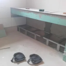 Konstrukcja z profili metalowych pod zabudowę, obłożona częściowo płytami gipsowo-kartonowymi, widoczne narzędzia i ochraniacze na kolana na podłodze.