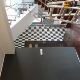 Bonabud - Ściana pomalowana na ciemny kolor w korytarzu ze schodami, widoczna drabina malarska i puszka farby, ściana z wzorem geometrycznym w tle.