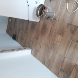 Bonabud - Fragment pomieszczenia w trakcie remontu: świeżo pomalowana ściana z widocznymi śladami po wcześniejszych pracach, podłoga wyłożona panelami imitującymi drewno, metalowe wiadro z odpadami budowlanymi.