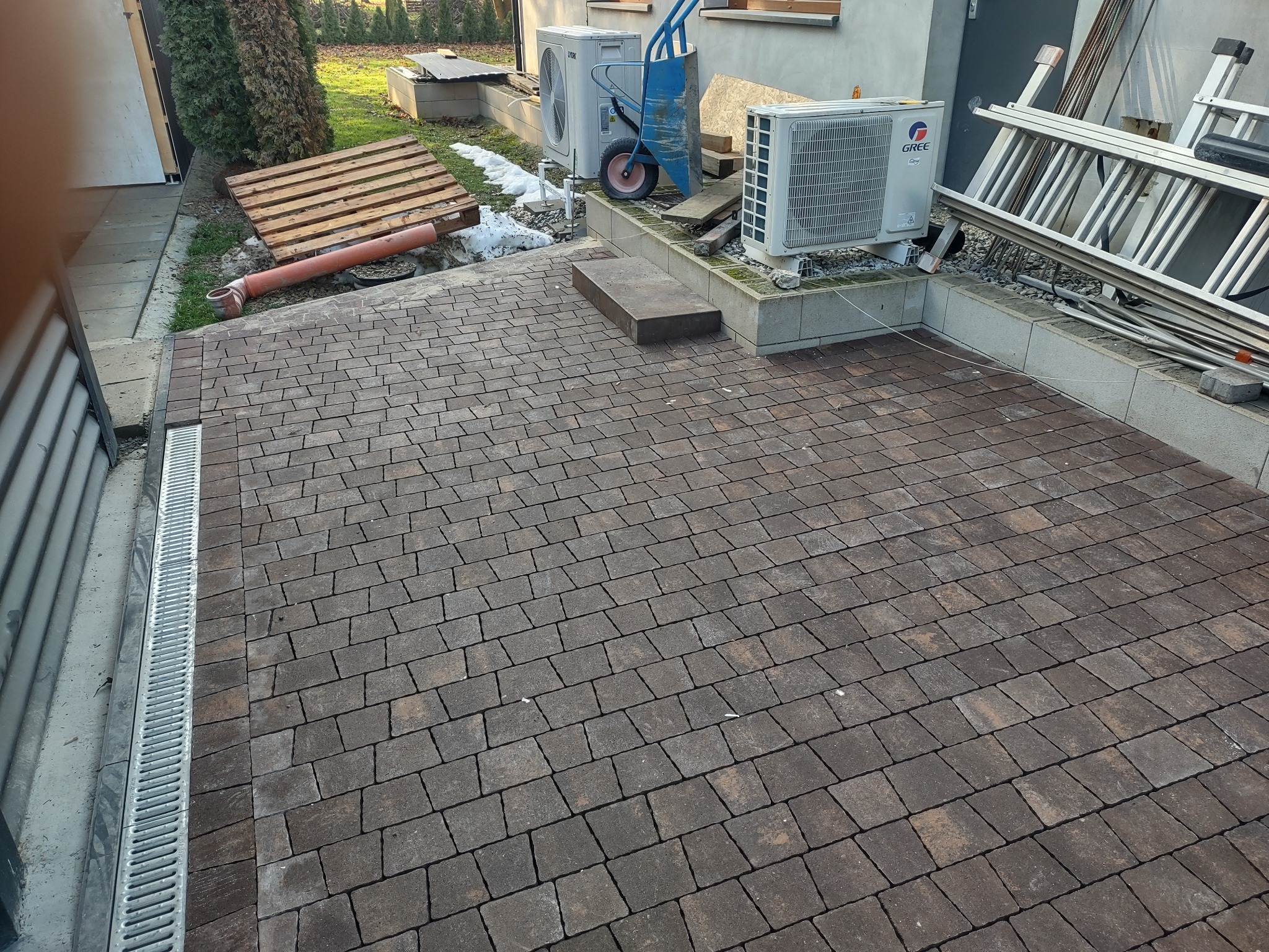 Ułożona kostka brukowa w Siedlcu z odpływem liniowym. W tle sprzęt budowlany i klimatyzatory. Widok na gotową nawierzchnię z kostki.