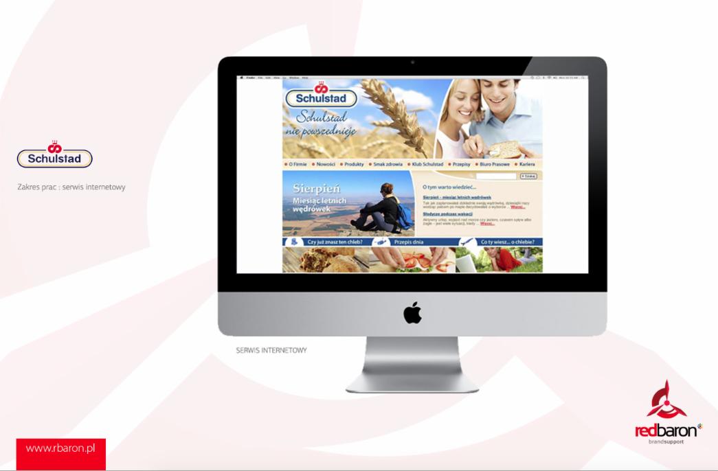 Ekran komputera iMac wyświetlający stronę internetową Schulstad z motywem pszenicy i pary jedzącej chleb, z logo Schulstad i Red Baron na tle.