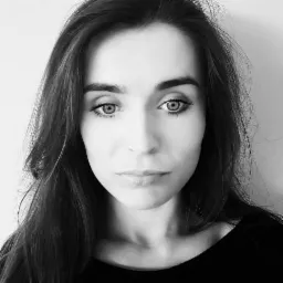 Portret kobiety z długimi, ciemnymi włosami, w czarno-białej tonacji, z wyraźnym spojrzeniem skierowanym wprost, na jasnym tle.