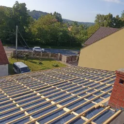 Wstępny etap budowy dachu w Pcimiu: widok na konstrukcję więźby z łatami i kontrłatami, na tle zieleni i błękitnego nieba.