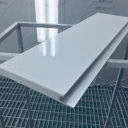 Biały, lakierowany blat na metalowym stelażu w lakierni, widoczne refleksy światła na powierzchni, kratka ściekowa w tle.