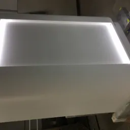 Biała, podświetlana od wewnątrz lada recepcyjna z zaokrąglonymi bokami, widoczny zasilacz i okablowanie w tle.