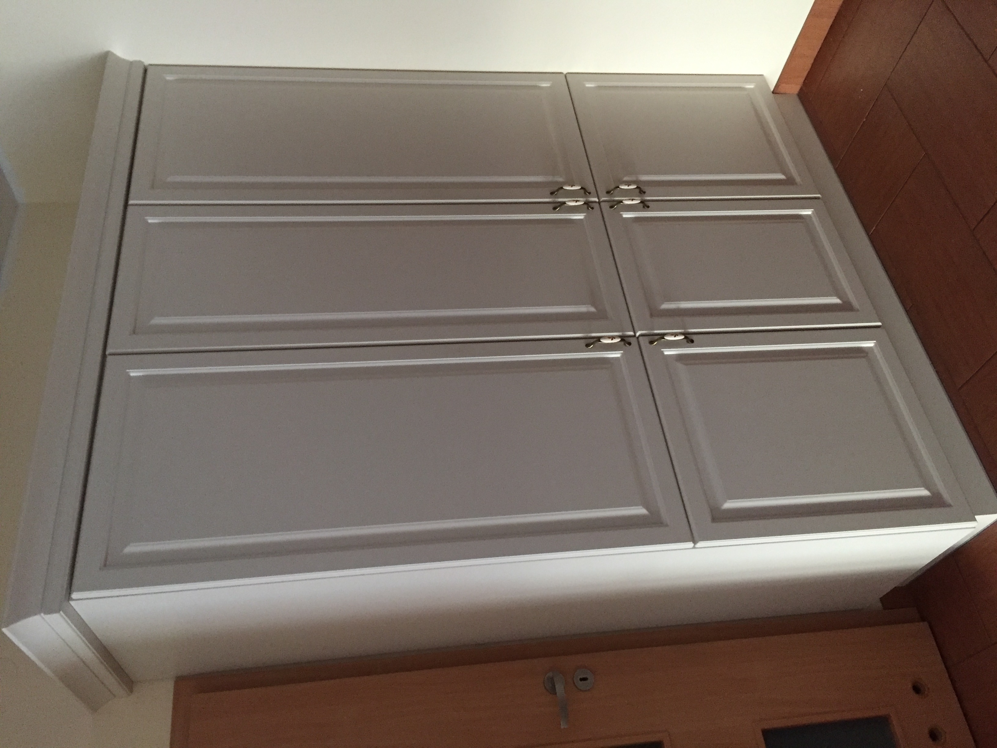 Szare szafki kuchenne podwieszane, z ozdobnymi listwami i chromowanymi uchwytami, zamontowane w domu w Czempiniu.