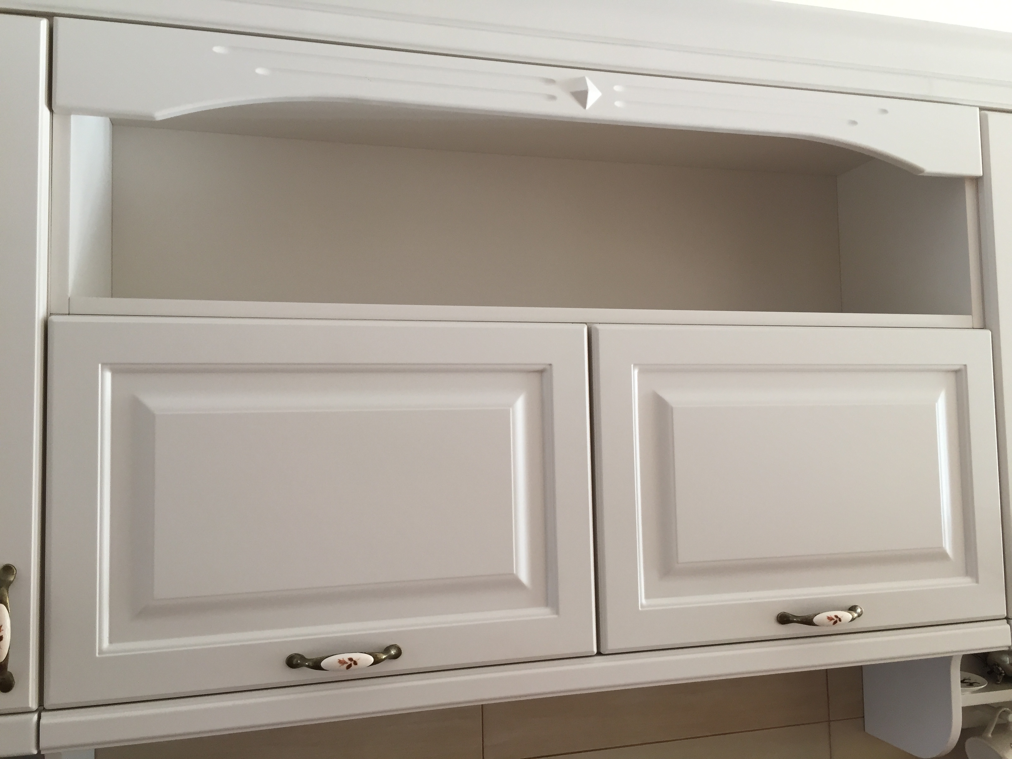 Białe szafki kuchenne z ozdobnymi uchwytami i otwartą półką powyżej, widoczne z bliska.