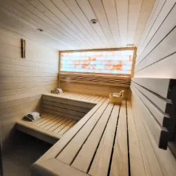 Wnętrze drewnianej kabiny z podświetlaną ścianą z bloków solnych, drewniane ławki z podgłówkami i wiaderko z akcesoriami.