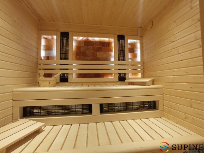 Wnętrze drewnianej kabiny z podświetlanymi panelami solnymi, drewnianym wiadrem i ławkami z grzejnikami pod spodem.