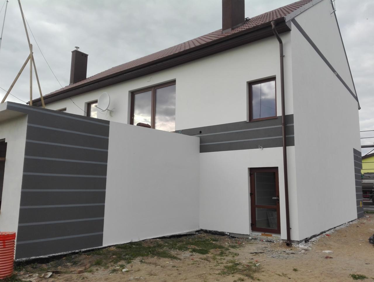 Nowoczesny dom z białą i szarą elewacją w poziome pasy, brązowe okna i dachówka, widoczna antena satelitarna i fragment rusztowania.
