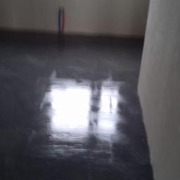 Usługi budowlane Wiesław Lisiecki - Położona, ciemna, błyszcząca glazura podłogowa w trakcie prac wykończeniowych, widoczne pionowe rury instalacyjne przy ścianie w tle.