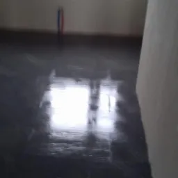 Położona, ciemna, błyszcząca glazura podłogowa w trakcie prac wykończeniowych, widoczne pionowe rury instalacyjne przy ścianie w tle.