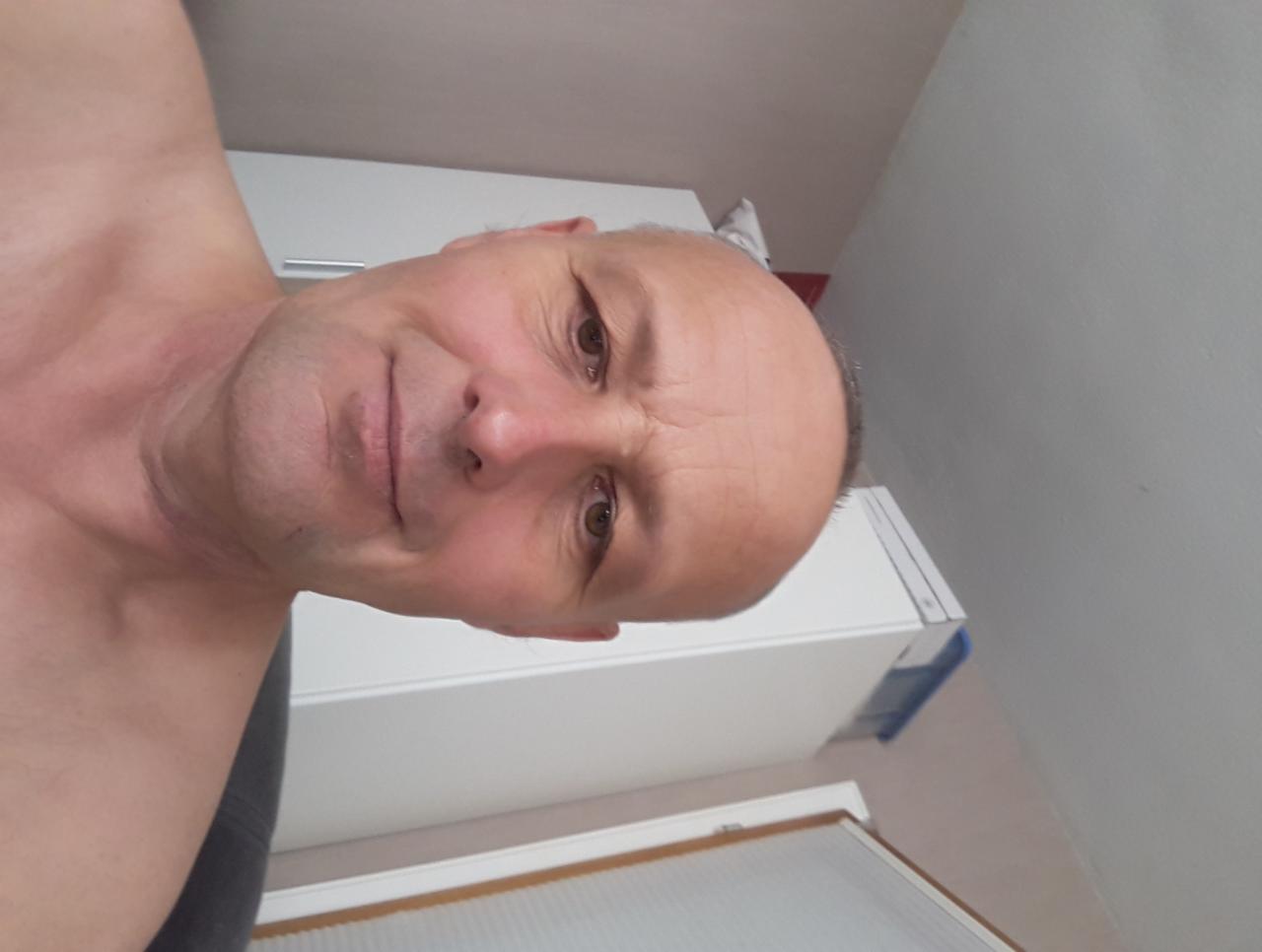 Autoportret mężczyzny z bliska, z białym szafką w tle, uchwycony pod nietypowym kątem.