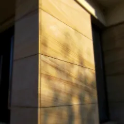 Fasada budynku wykończona piaskowcem w formie prostokątnych płyt, oświetlona ciepłym światłem słonecznym, widoczny fragment okna i logo firmy w górnym rogu.