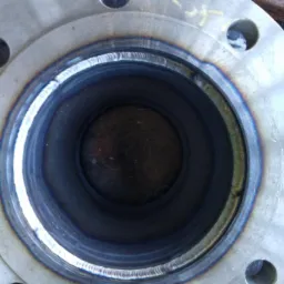 Spoina wewnątrz metalowego kołnierza, widoczne ślady termiczne na metalu.