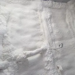 Świeżo nałożona, biała izolacja natryskowa pokrywa ścianę, obejmując metalowy uchwyt na wąż.