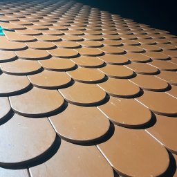 SŁAWOMIR WOJTUSZKIEWICZ - Nowy dach pokryty brązową dachówką bitumiczną w kształcie łuski, ułożoną równo i pod kątem, z widocznym fragmentem zielonej membrany w rogu.