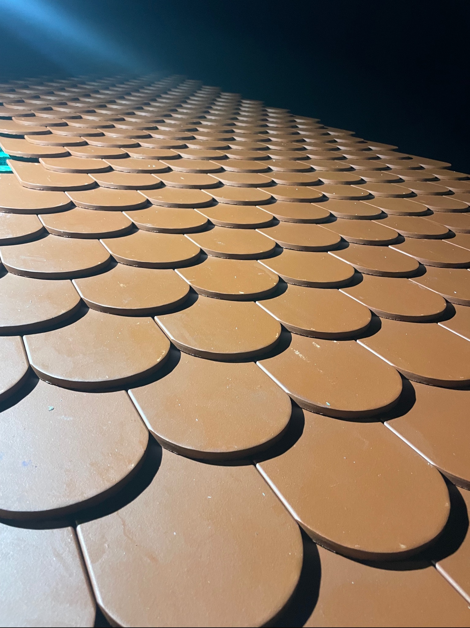 Nowy dach pokryty brązową dachówką bitumiczną w kształcie łuski, ułożoną równo i pod kątem, z widocznym fragmentem zielonej membrany w rogu.