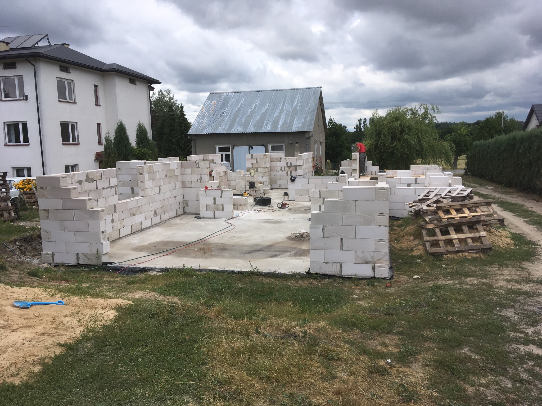 Budowa domu z betonu komórkowego w Urzędowie. Widoczne ściany fundamentowe i narzędzia budowlane. Prace murarskie w toku, palety z bloczkami obok.