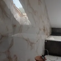 Wykończona łazienka na poddaszu z oknem dachowym, ściany wyłożone płytkami imitującymi marmur, obudowa wanny wykończona czarną mozaiką heksagonalną, widoczne narzędzia glazurnicze.