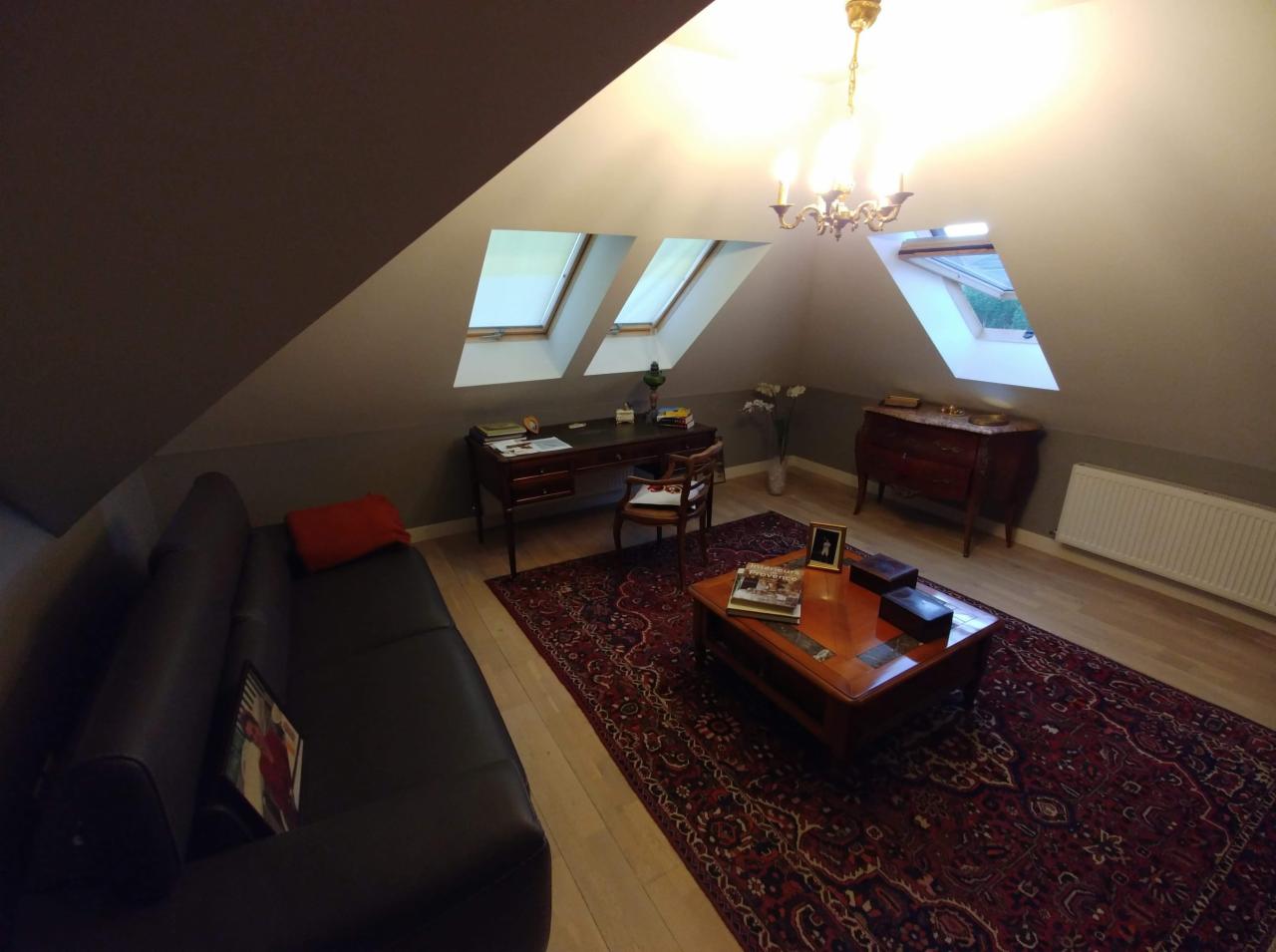 Pokój na poddaszu z oknami dachowymi, biurkiem, komodą i kanapą, wykończony w klasycznym stylu.