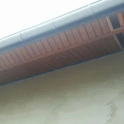 Montaż drewnopodobnej podbitki dachowej z widocznym fragmentem konstrukcji dachu i orynnowaniem, ujęcie z dołu