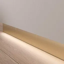 Detal minimalistycznego wnętrza: drewniana podłoga, biała ściana z zamontowaną złotą listwą przypodłogową z podświetleniem LED.