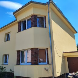 USŁUGI OGÓLNOBUDOWLANE IGOR KOŁODZIEJ BUDIGO - Żółty dom jednorodzinny z ceglanymi elementami dekoracyjnymi wokół okien, świeżo po malowaniu, widoczne ślady prac na podjeździe.