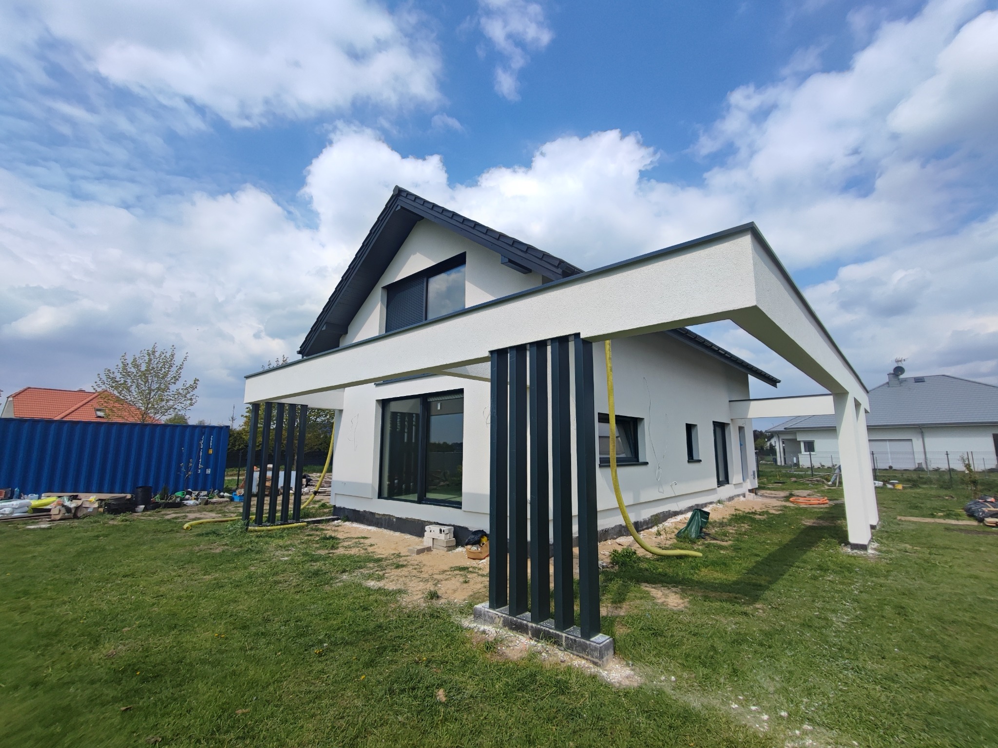 Nowoczesny dom jednorodzinny z jasną elewacją i czarnymi elementami konstrukcyjnymi w Szczecinie, widoczny podczas prac wykończeniowych.