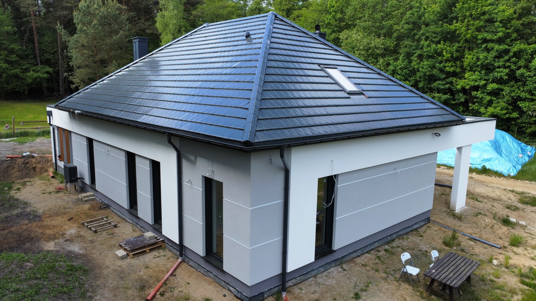 Nowoczesny dom jednorodzinny z szarą elewacją i grafitowym dachem, widoczny z góry, z elementami wykończeniowymi i otoczeniem w trakcie aranżacji.