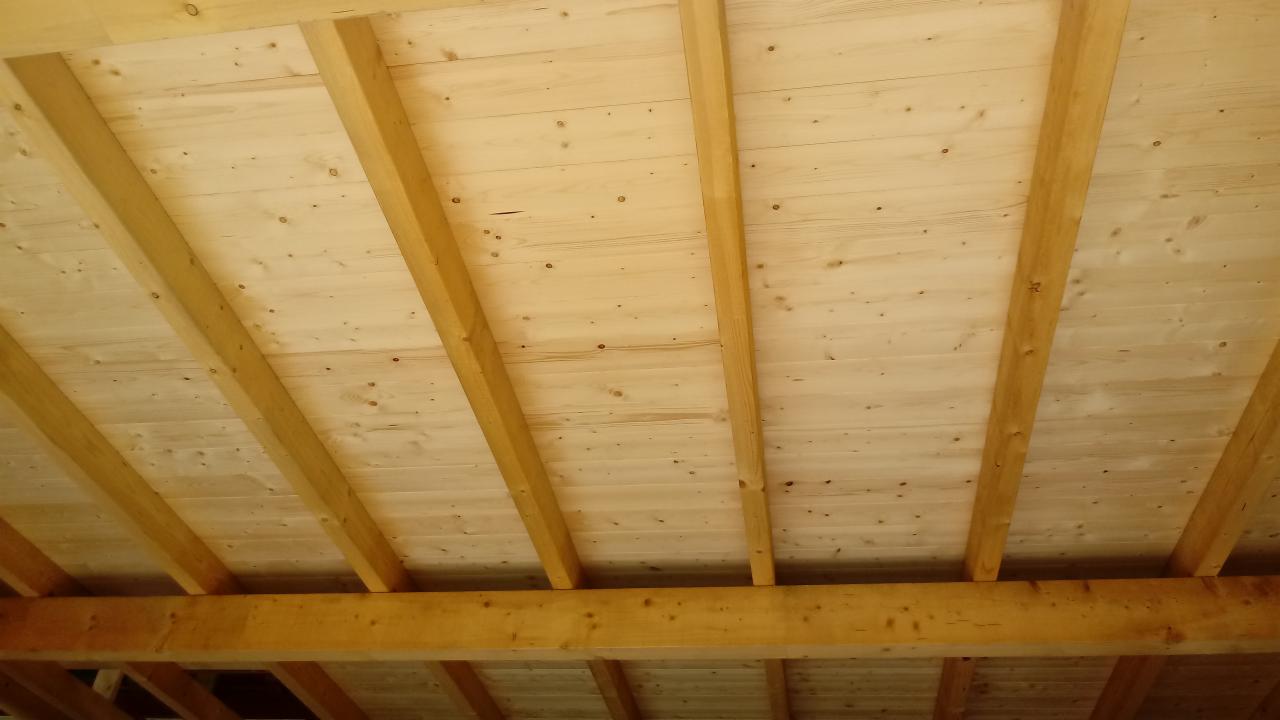 Drewniana konstrukcja dachu z widocznymi belkami i deskowaniem, surowe drewno o jasnym odcieniu, widok od dołu.