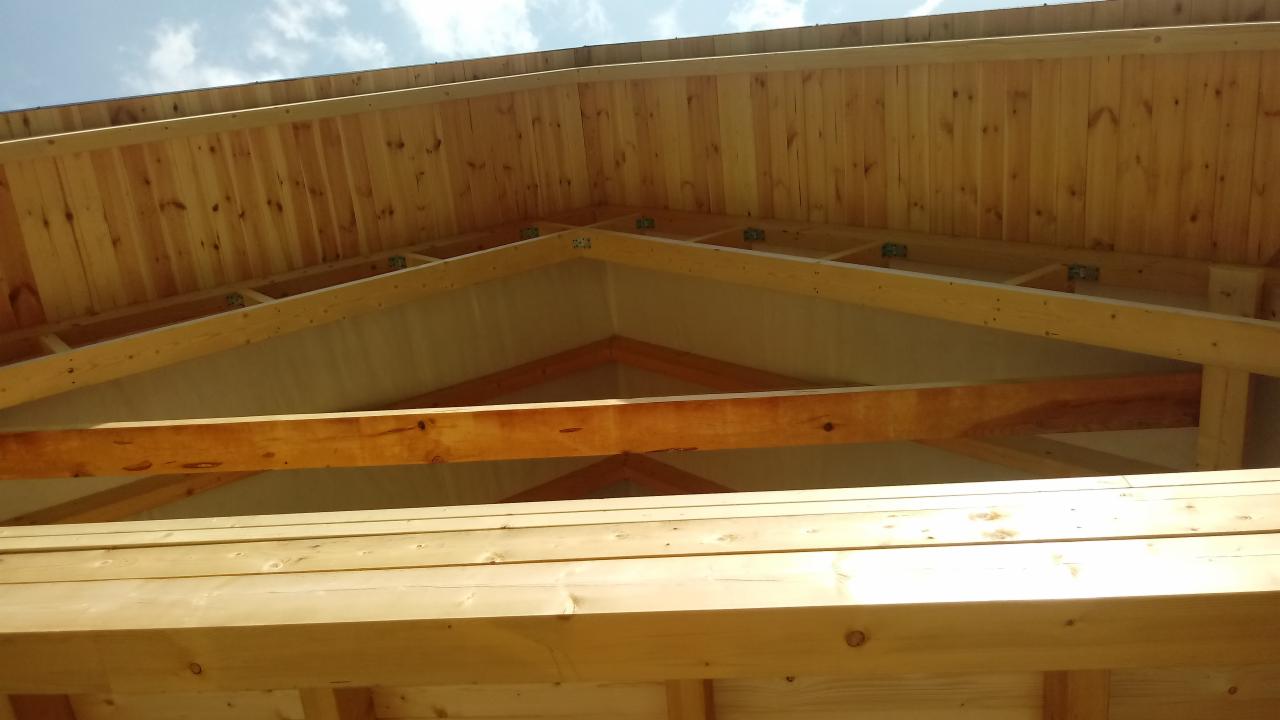 Wnętrze konstrukcji drewnianej dachu z widoczną więźbą i deskowaniem, jasne drewno, kąt widzenia od dołu.