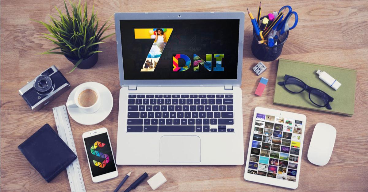 Biurko z laptopem wyświetlającym graficzne logo '7 DNI', obok filiżanka kawy, aparat, tablet z miniaturkami stron, telefon z kolorowym logo i przybory biurowe.