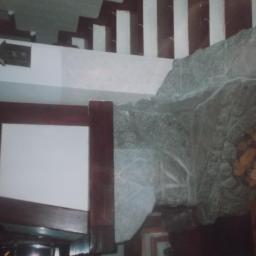 Abra-bud - Fragment wnętrza z dekoracyjnym obłożeniem kamiennym ściany, drewnianymi elementami konstrukcyjnymi i schodami w tle.